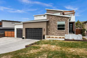 Contemporary home featuring stone siding, driveway, and a garage