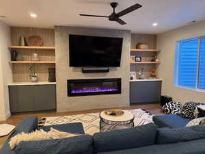 Living area featuring a large fireplace, a ceiling fan, built ins, and light wood finished floors