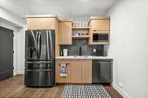 Kitchenette featuring stainless steel refrigerator with ice dispenser, modern cabinets, dishwasher, light wood finish cabinetry, and open shelves