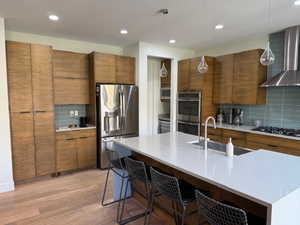 Kitchen with wall chimney exhaust hood, backsplash, hanging light fixtures, stainless steel appliances, and recessed lighting