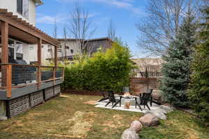 View of grassy yard featuring a patio area, a wooden deck, and an outdoor fire pit
