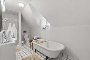 Full bathroom with a freestanding tub, lofted ceiling, a shower stall, and light tile patterned floors