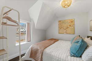 A bedroom with a lofted ceiling, wood-finished floors, and a king bed.