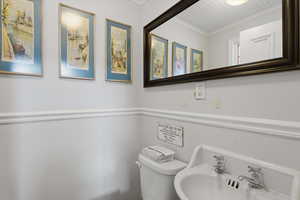 Half bath featuring ornamental molding and a toilet off the kitchen.