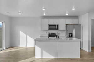 Kitchen featuring white cabinets, stainless steel appliances, recessed lighting, light wood-style flooring, and a kitchen island with sink