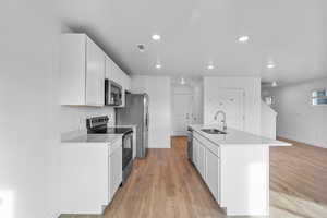 Kitchen featuring appliances with stainless steel finishes, white cabinetry, a kitchen island with sink, light stone counters, and light wood finished floors