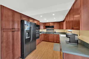 Kitchen featuring recessed lighting, black appliances, light wood-type flooring, brown cabinets, and under cabinet range hood