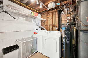 Washroom featuring unfinished concrete floors, heating unit, and washer and clothes dryer
