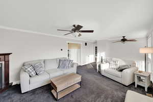 Living area with ornamental molding, carpet flooring, a fireplace, and a ceiling fan