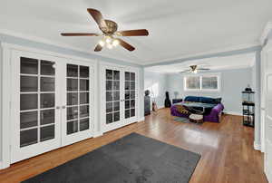 Living room with ornamental molding, wood finished floors, french doors, and a ceiling fan