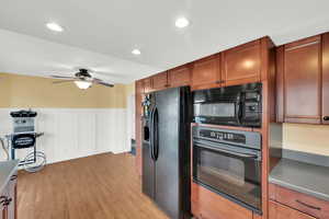 Kitchen featuring wainscoting, black appliances, a decorative wall, light wood-type flooring, and brown cabinetry