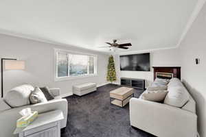 Living room featuring ornamental molding, dark carpet, and ceiling fan