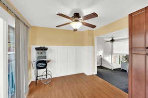 Spare room with healthy amount of natural light, wainscoting, a decorative wall, wood finished floors, and a ceiling fan