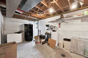 Unfinished below grade area featuring fridge and black refrigerator with ice dispenser