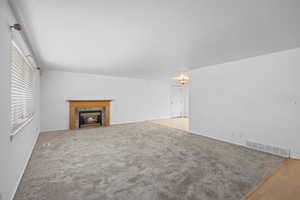 Unfurnished living room featuring a fireplace, a textured ceiling, and light colored carpet