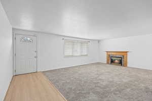 Unfurnished living room featuring a tiled fireplace, a textured ceiling, and wood finished floors