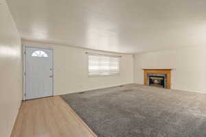 Unfurnished living room with a textured ceiling, a tile fireplace, and wood finished floors