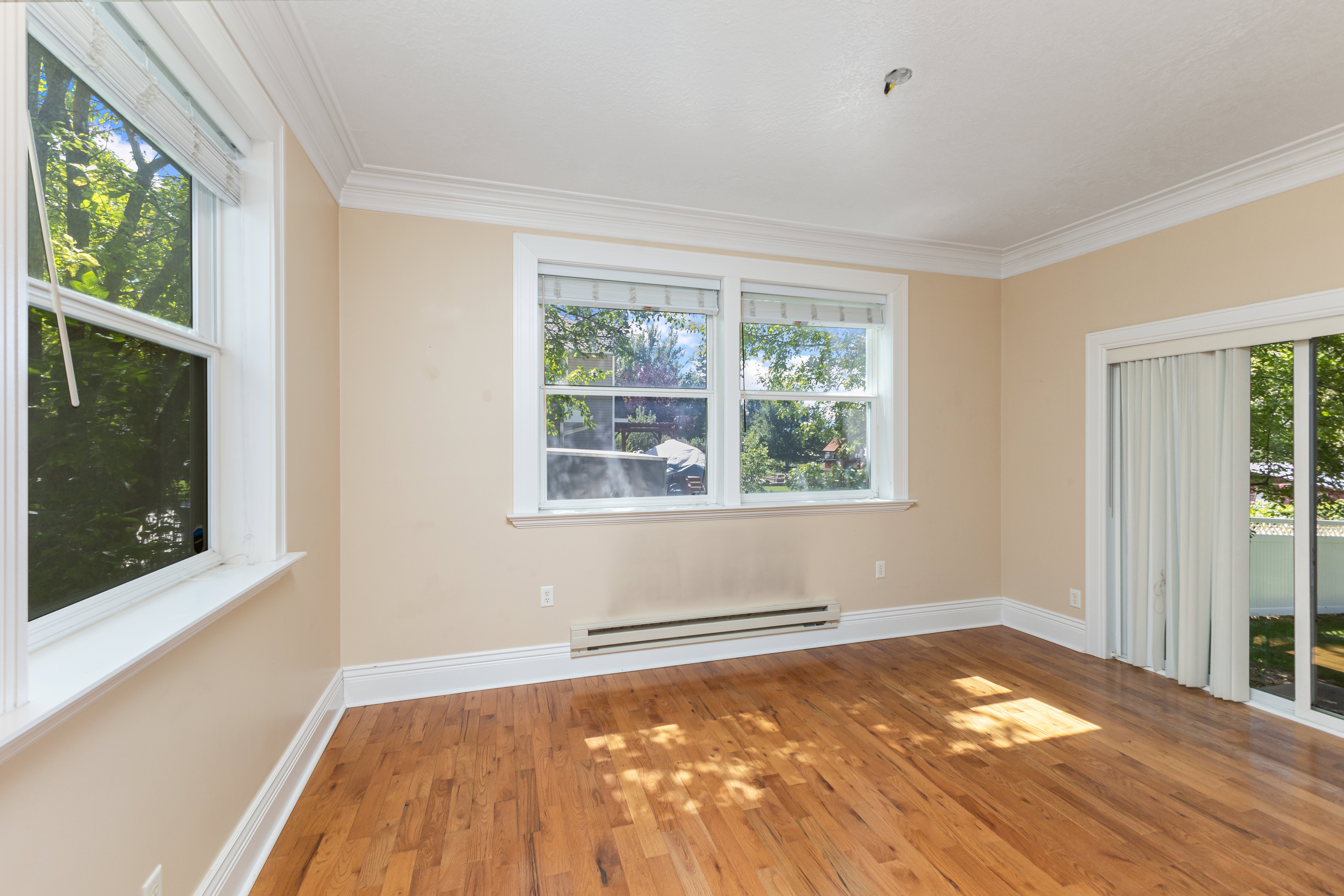 Empty room with a baseboard heating unit, wood finished floors, and crown molding