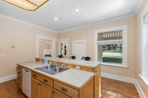 Kitchen featuring light countertops, an island with sink, white dishwasher, dark wood-style floors, and crown molding