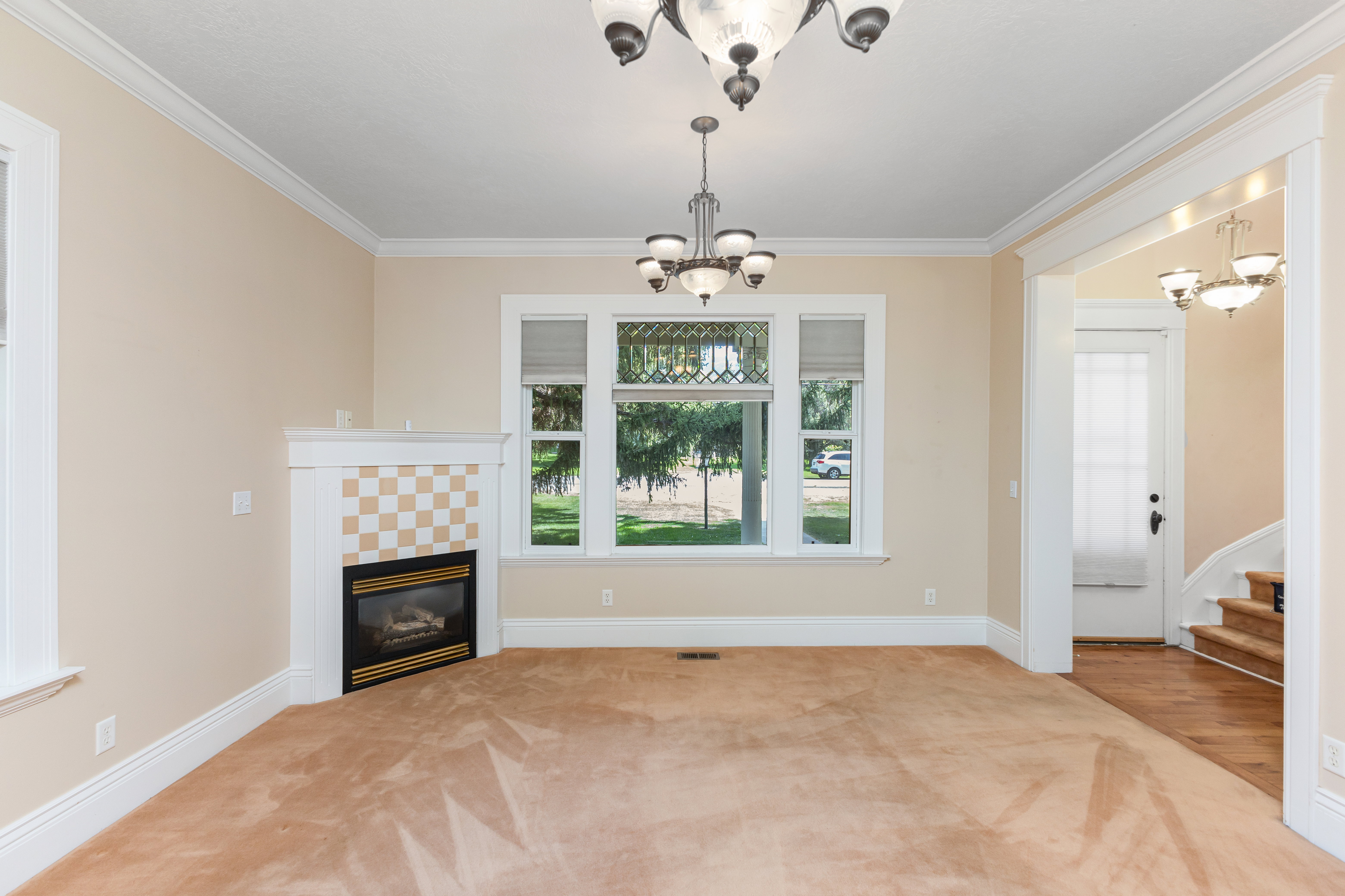 Unfurnished living room featuring a chandelier, ornamental molding, a tiled fireplace, light carpet, and stairs