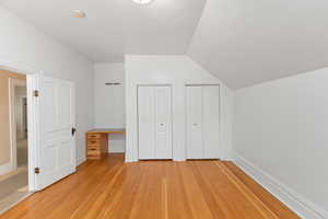 Unfurnished bedroom with multiple closets, vaulted ceiling, light wood-type flooring, and built in desk