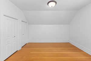 Additional living space with light wood-style floors and vaulted ceiling
