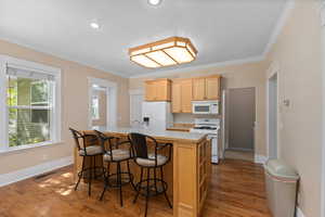 Kitchen with light countertops, crown molding, white appliances, an island with sink, and a kitchen bar