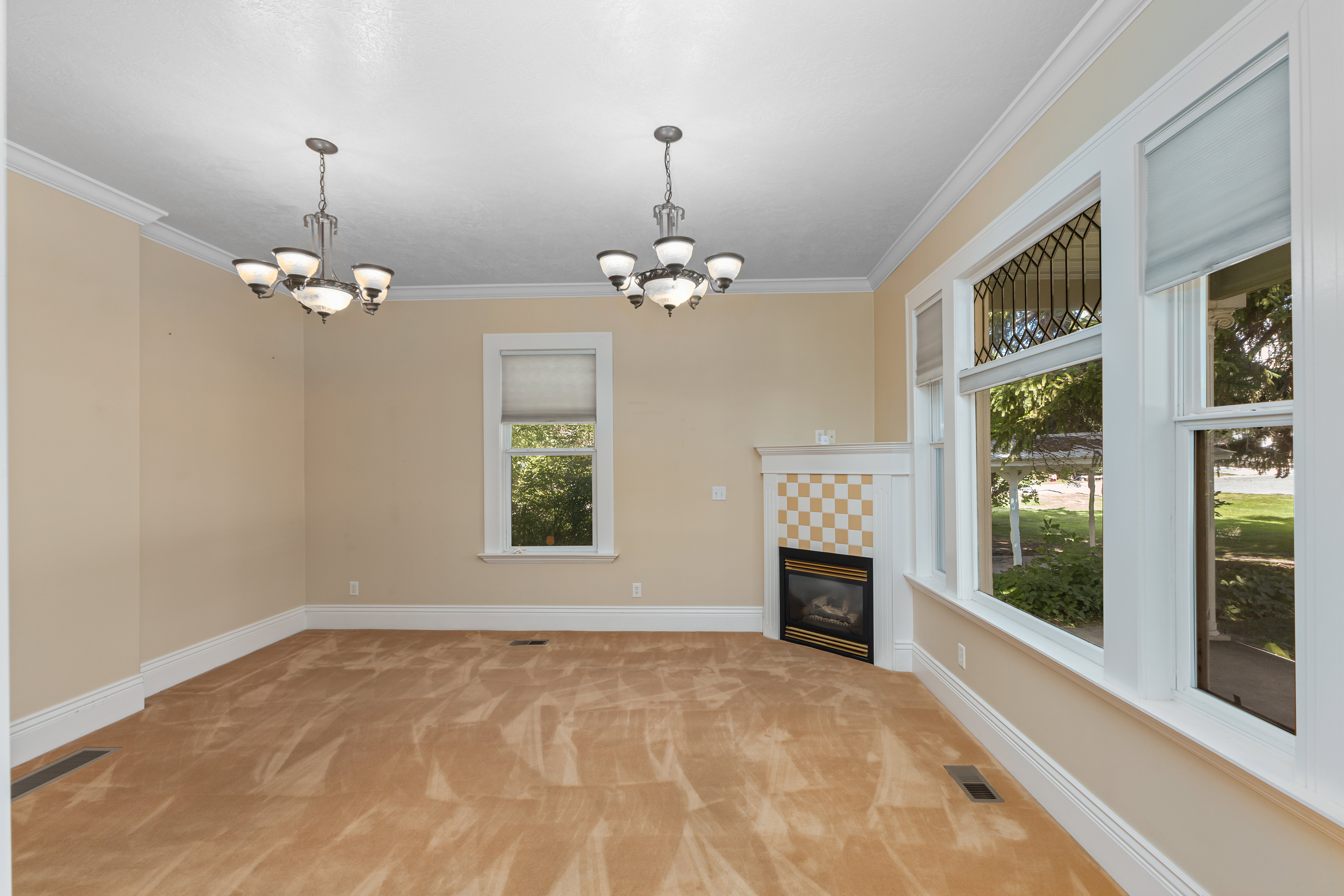 Unfurnished living room featuring light carpet, ornamental molding, a tile fireplace, and a chandelier