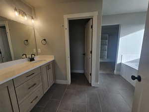Bathroom with vanity, dark tile patterned floors, and tiled bath