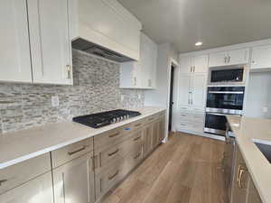 Kitchen with white cabinets, custom exhaust hood, appliances with stainless steel finishes, recessed lighting, and light wood-style flooring