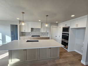 Kitchen with hanging light fixtures, a textured ceiling, a kitchen island with sink, light stone counters, and recessed lighting