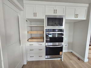 Kitchen featuring white cabinets, stainless steel appliances, light wood-type flooring, and open shelves