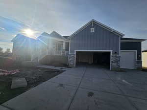 View of front facade with a porch, stone siding, a garage, and driveway