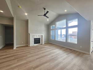 Unfurnished living room featuring light wood-style flooring, a stone fireplace, ceiling fan, recessed lighting, and high vaulted ceiling