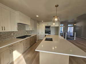 Kitchen featuring a center island with sink, white cabinetry, decorative light fixtures, light wood-style flooring, and light stone counters