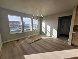 Unfurnished dining area featuring a chandelier, light wood finished floors, and a textured ceiling