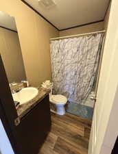 Bathroom featuring dark wood-type flooring, vanity, ornamental molding, and shower / bath combo with shower curtain