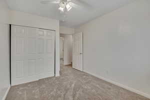 Unfurnished bedroom featuring light carpet, a closet, and a ceiling fan