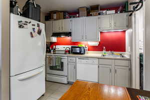 Kitchen featuring white appliances, light tile patterned flooring, light countertops, and under cabinet range hood