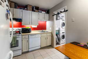 Kitchen with white appliances, light countertops, stacked washing machine and dryer, ventilation hood, and light tile patterned floors