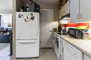 Kitchen with white appliances, light countertops, white cabinetry, under cabinet range hood, and light tile patterned flooring