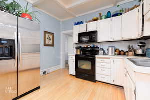 Kitchen with black appliances, white cabinets, light countertops, and light wood-style floors