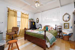 Bedroom featuring beam ceiling, coffered ceiling, wood finished floors, and a ceiling fan
