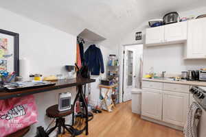 Kitchen with white cabinetry, light countertops, white range oven, light wood finished floors, and vaulted ceiling