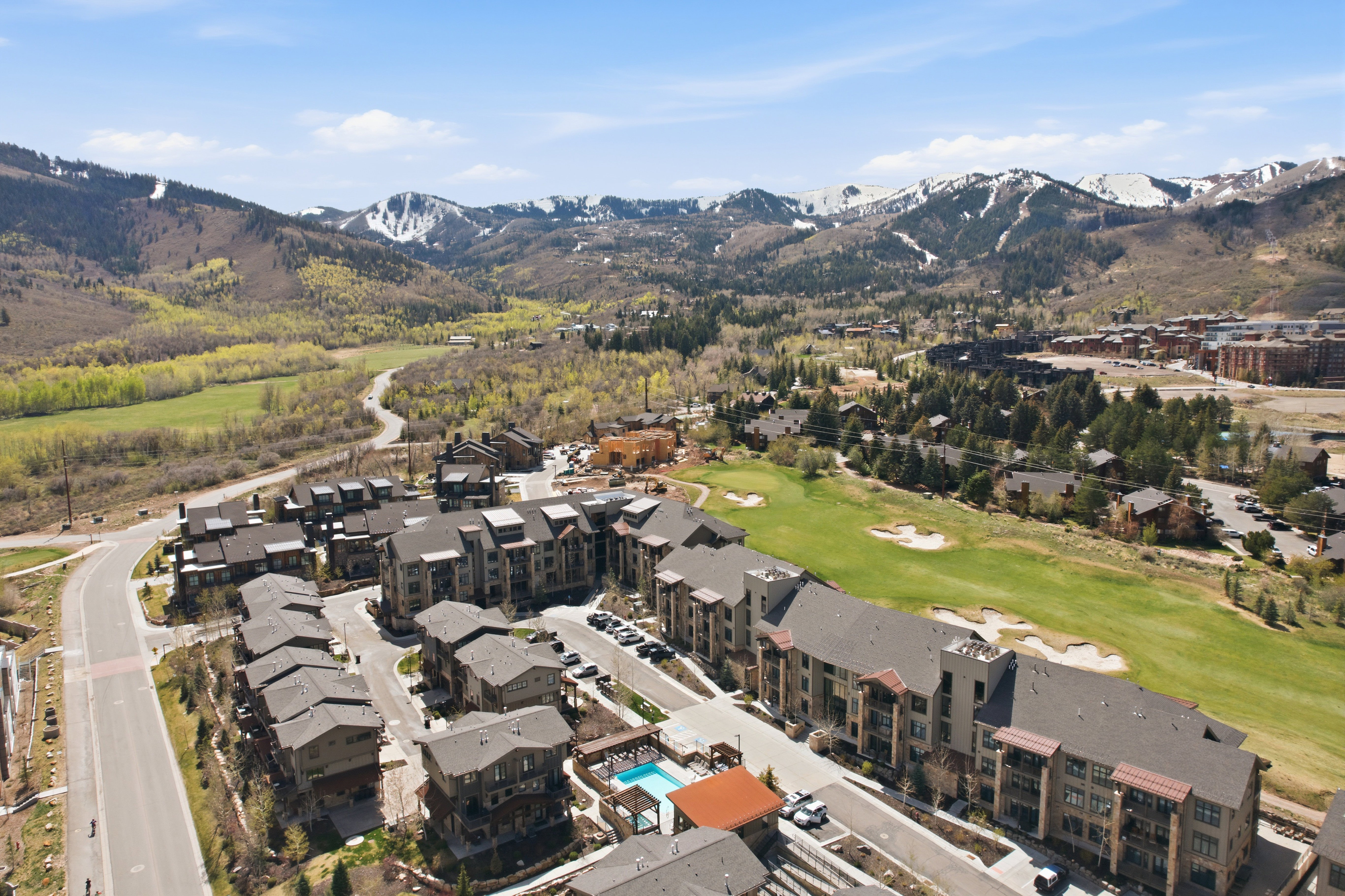 Community of multi-story buildings with balconies, featuring an outdoor pool and adjacent golf course