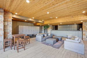 Spacious communal area featuring a wood-panel ceiling, stone accent walls, recessed lighting, and large format tile flooring