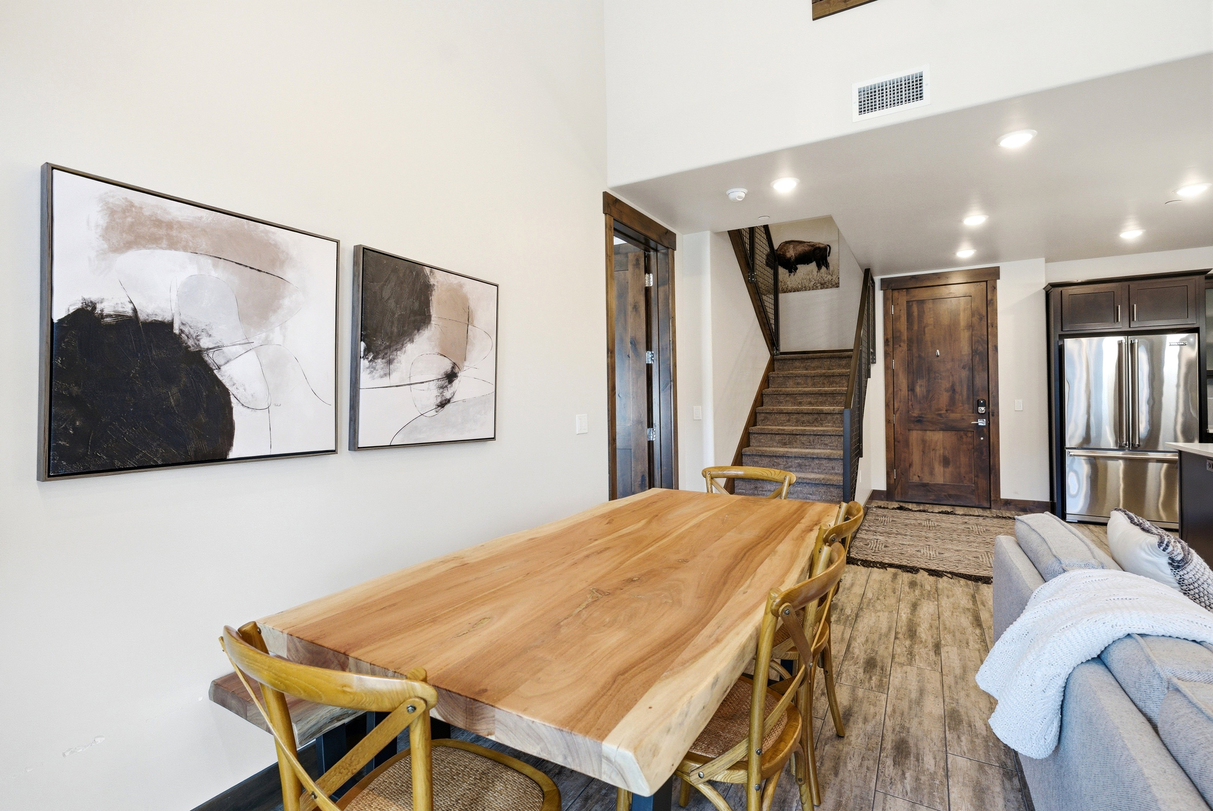 Open-concept living area featuring high ceilings, recessed lighting, wood-finish flooring, a contemporary dining table, and a built-in stainless steel refrigerator