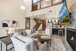 Spacious open-concept living area featuring high ceilings, a stacked stone fireplace, wood-finish flooring, and a second-story interior balcony with metal railing