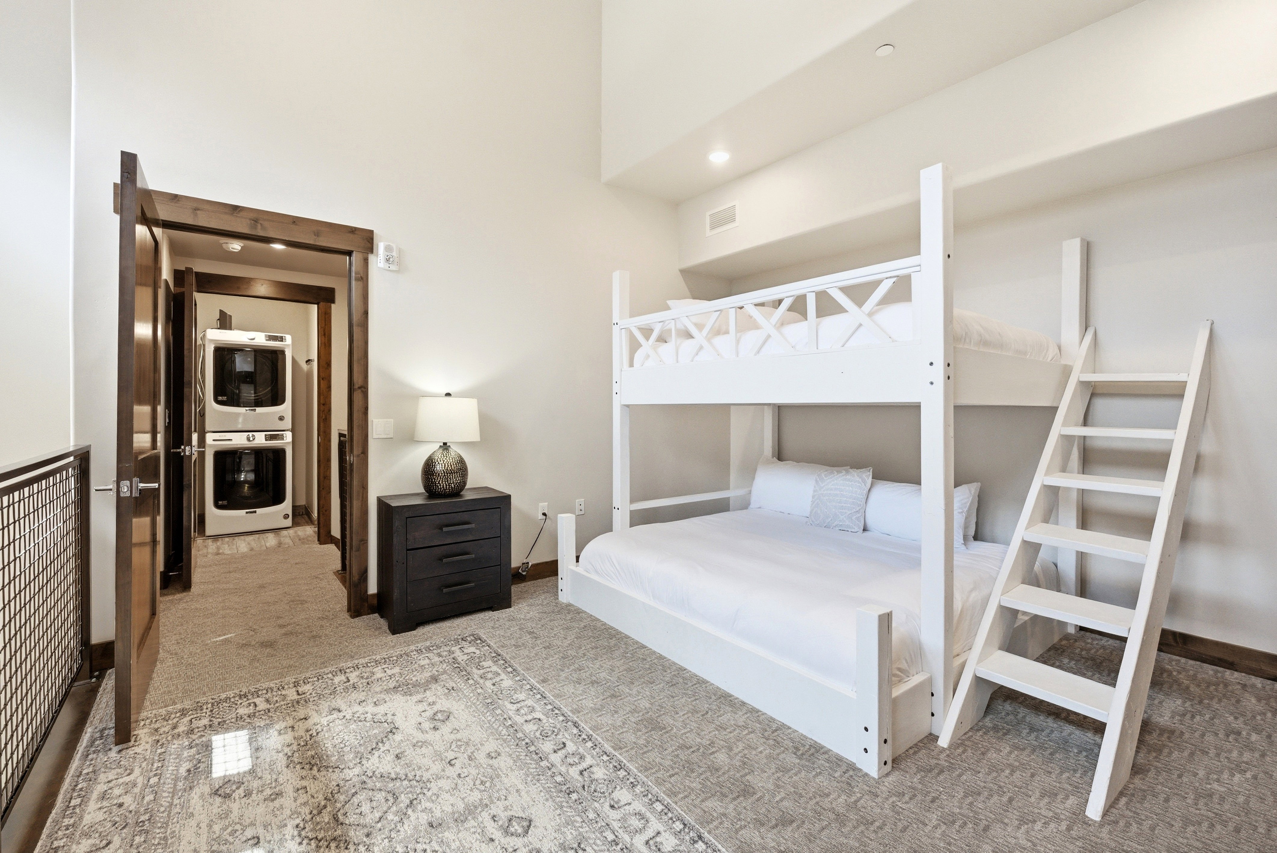 Carpeted room featuring a built-in bunk bed, an adjacent doorway with a stacked washer and dryer, and a dark wood-finish nightstand
