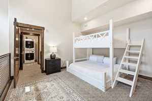 Carpeted room featuring a built-in bunk bed, an adjacent doorway with a stacked washer and dryer, and a dark wood-finish nightstand